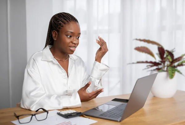 African american businesswoman have video conference with business partners, young black lady in formal outfit sitting at home office, using computer pc laptop, looking at screen and gesturing