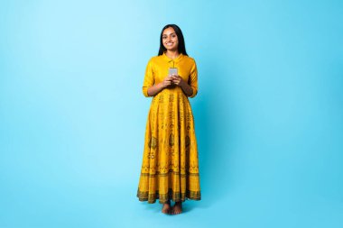 Mobil Teklif. Geleneksel Elbise Giyen Hintli Kadın Mavi Stüdyo Arkaplanda Akıllı Telefon Kullanıyor. Genç Ortadoğulu Bayan İnternet 'e Telefon Gadget' ında Mesajlaşıyor ve Taranıyor