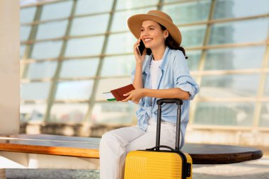 Şapkalı, şapkalı, pasaportu ve bileti olan gülümseyen beyaz kadın tren istasyonundan, havaalanından arıyor. Trip ve yaşam tarzı, seyahat, iletişim, aygıt