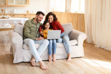 Evde dizüstü bilgisayar kullanan, internette sörf yapan ya da modern oturma odasındaki kanepede otururken görüntülü sohbet yapan Latin kökenli genç bir ebeveyn ve kız. Online teklifler, teknoloji