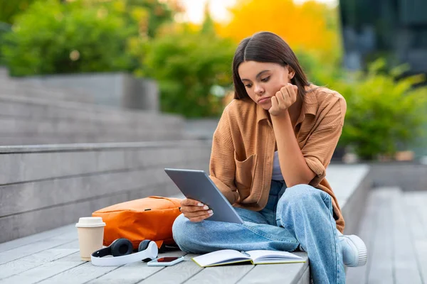 公園の階段に一人で座り デジタルタブレットを持ち 宿題をする若い女性大学生は プロジェクトに困難を抱えています 悲しい女性が孤独で空虚な空間を感じる — ストック写真