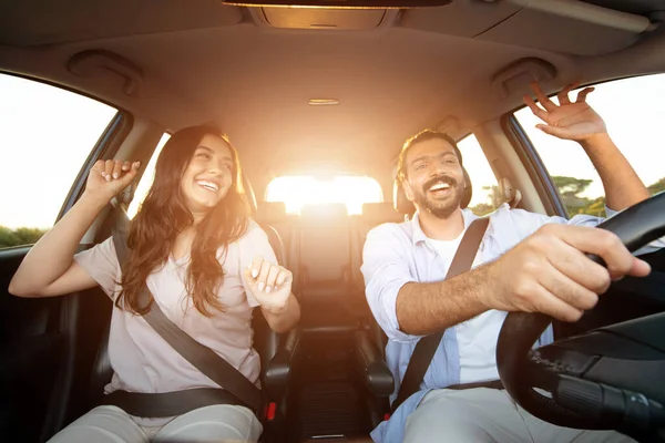 Active leisure, car trip concept. Positive young latin couple husband and wife having fun while driving auto, listening to music and dancing, shot from dashboard