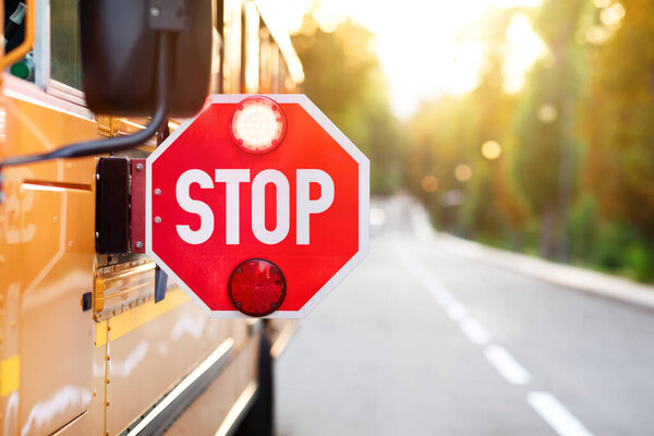 Желтый школьный автобус с красным знаком "стоп", стоящий на дороге, крупный план знака внимания со световым сигналом висящим на школьном автобусе, транспортные средства для концепции школьников, копировальное пространство