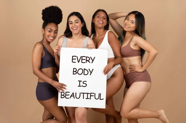 Positive diverse women in different underwear, posing and enjoying natural beauty, holding banner inscription every body is beautiful, isolated on beige background