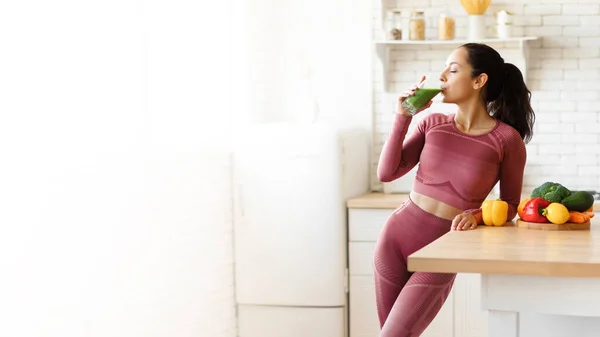 Healthy Nutrition. Young Sporty Lady In Fitwear Drinking Glass Of Green Smoothie In Kitchen, Panorama With Copy Space For Text. Woman Enjoying Healthy Detox Drink Slimming On A Weight Loss Diet