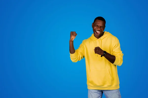 陽気で興奮する若い黒人男性が勝利を祝い 手でサクセスサインを作り 青い背景 スタジオで孤立した勝利を楽しんでいます オファー 良いニュース反応 ライフスタイル — ストック写真
