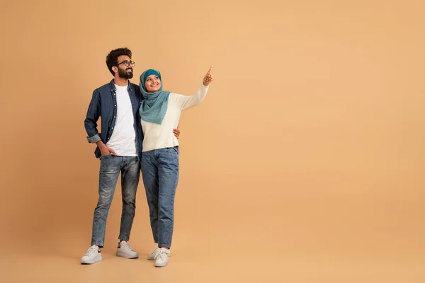 これをチェック 若いムスリムのカップルは コピースペース アラブの男とヒジャブで あなたの広告やオファーのための無料の場所を表示し ベージュの背景に一緒に立って 完全な長さ — ストック写真