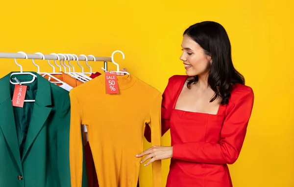 ハッピーエキサイティングな若い女性が割引タグで新しい服をデモンストレーション トレンドのTシャツと赤の販売タグで美しい女性ホールディングハンガーを笑顔 イエロースタジオの背景に孤立 — ストック写真