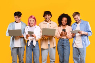 Uzaktan eğitim için modern aletler. Telefon, tablet ve dizüstü bilgisayarları olan mutlu öğrenci arkadaşları sarı arka planda izole edilmiş poz veriyorlar.