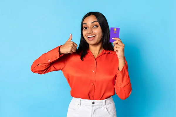 Great Financial Offer. Happy Young Indian Woman Showing Bank Credit Card And Thumbs Up Gesture Over Blue Studio Background. Customer Advertising Cashback And Payment Service