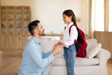 Okula geri dön. Sevgi dolu bir baba okul günü için sırt çantasıyla liseli kız çocuğunu hazırlıyor, ellerini tutuyor ve sabahları evde derslerin keyfini çıkarmaya teşvik ediyor.