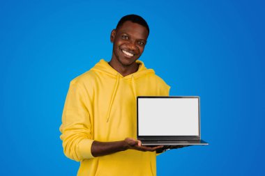 Mavi arka planda, stüdyoda izole edilmiş, boş ekranlı, mutlu genç siyahi öğrenci dizüstü bilgisayarı. Cihaz, web sitesi tavsiyesi, modern işletme ile uzaktan çalışma