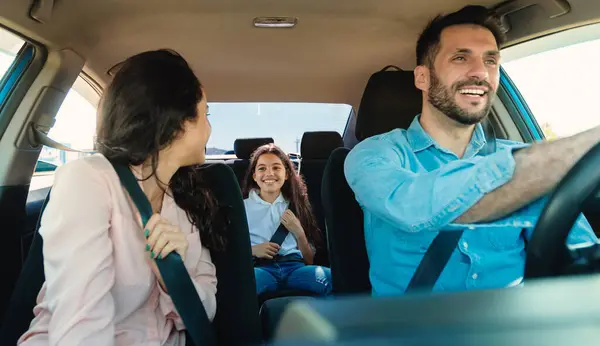 Happy parents and daughter sitting in auto during road trip, woman turning back to child, view from auto dashboard. Family traveling by automobile