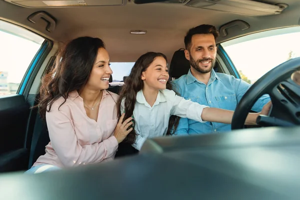 快乐的父母和他们的孩子享受着全新的汽车 女孩触摸方向盘 与父母坐在车内 从汽车仪表盘上看 — 图库照片
