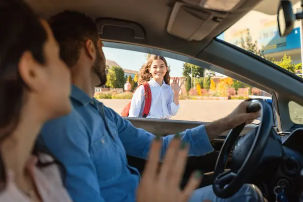 快乐的父母带着女儿上学 坐在车里 向小女孩挥手 在从车上进学校之前 父母向孩子告别 — 图库照片