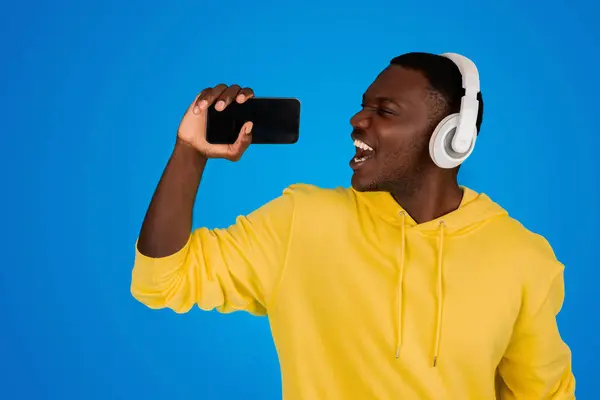 Happy Young Black Guy Wireless Headphones Sings Smartphone Empty Screen — Stock Photo, Image