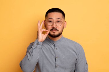 Sessiz ol. Fermuarlı Ağız Hareketi Yapan Genç Asyalı Adam, Parmaklarını Dudaklara Yakın Tutan, Ciddi Milenyum Erkek Tutma Sırrı, Sarı Stüdyo Arkaplanı Üzerinde İzole Edilmiş, Boşluğu Kopyala