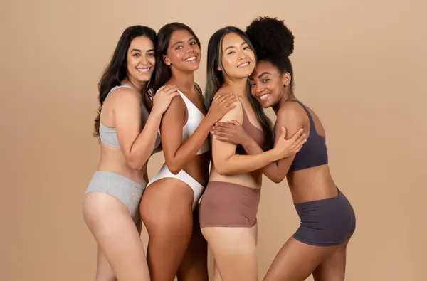 Happy young diverse women in different underwear, body types, posing and enjoying natural beauty, standing on beige background. Diversity, health care, support