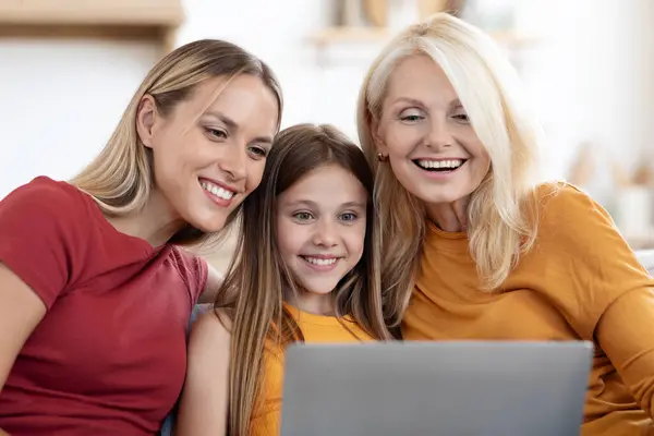 Happy caucasian family three generations mother, daughter and grandmother sitting on couch at home, using laptop, shopping online, websurfing on Internet, closeup. Family offer, online deal