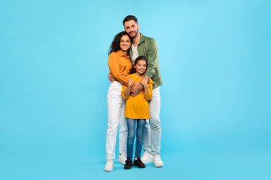 Sağlıklı bir aile ilişkisi. Avrupalı baba ve anne kızını kucaklıyor, mavi stüdyo arka planında poz veriyor, tam boy portre, serbest alan