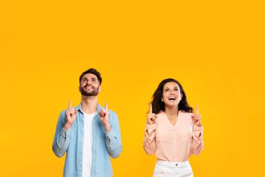 Heyecanlı Avrupalı erkek ve kadın rahat kıyafetlerle fotokopi alanına bakıyor ve onları işaret ediyor. Güzel bir teklif ya da anlaşma sunuyor. Tasarım ve reklamınız için yer, sarı arka plan.