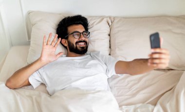 Mutlu Hintli genç adam evde yatakta uzanmış, elinde modern cep telefonu olan, gülümseyen bir doğu erkeği arkadaşlarıyla internet sohbeti yapıyor.