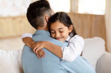 Genç ortadoğulu baba ve küçük tatlı kızının portresi. Evin içinde poz veriyor, reşit olmayan kız babasına gözleri kapalı sarılıyor. Baba konseptiyle mutlu bir ilişki
