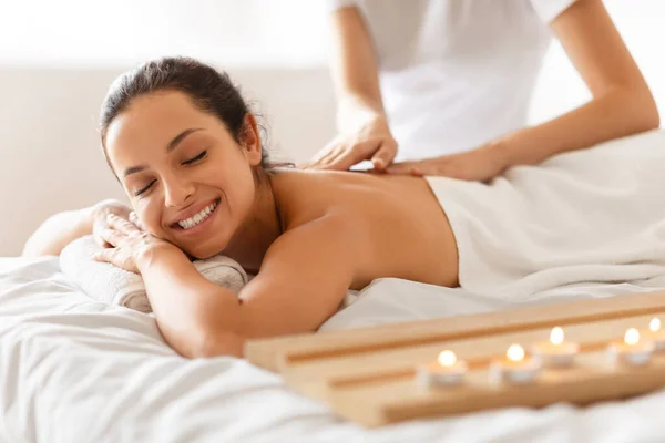 Young Woman During Massage Relaxing And Enjoying Procedure Lying On Bed In Spa Beauty Salon, Receiving Professional Back Massage From Masseur, Posing With Eyes Closed. Wellness, Relaxation Therapy