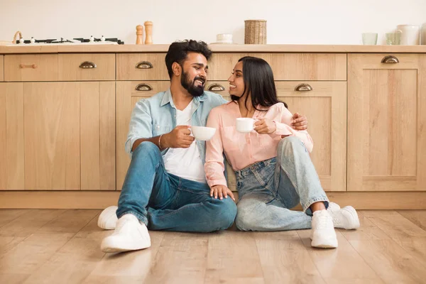 インドのカップルが一緒に朝のコーヒーを飲んで愛し 自宅のキッチンで床に座って ロマンチックな配偶者がホットドリンクを楽しんで 抱擁し お互いを見つめあい 無料のスペース — ストック写真
