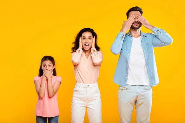 Hear no evil, see no evil, speak no evil. Family of three people covering eyes, ears and mouth, showing blind, deaf and three wise monkey scene, posing over yellow background