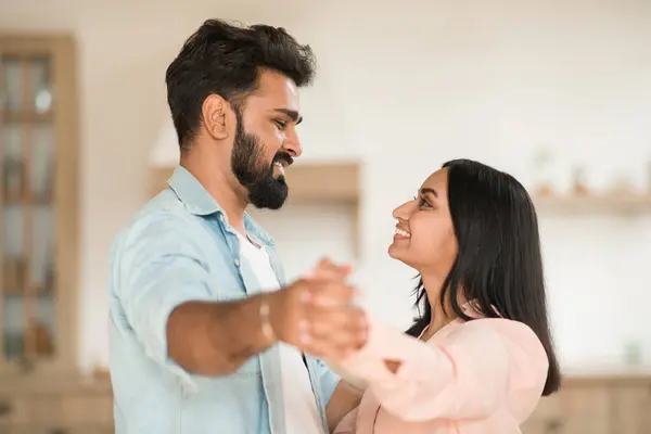 Romantic indian couple enjoying time together at home, dancing waltz, loving spouses holding hands and smiling to each other, enjoying happy moment, copy space, side view