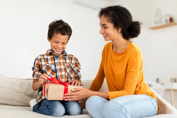 给男孩的生日礼物 可爱的妈妈问候小儿子给了他包装好的礼品盒 一起在家里庆祝节日 坐在沙发上 孩子出生时快乐的母亲带来惊喜 — 图库照片