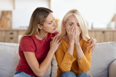 Kızını önemseyen, hayal kırıklığına uğramış yaşlı bir kadını rahatlatan, kucaklayan, evdeki koltukta oturan, kendini iyi hissetmeyen yaşlı bir kadını üzen, ağlayan, yüzünü kapatan, depresyondan muzdarip, kederli bir kadın.