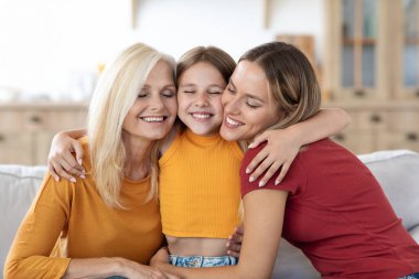 Mutlu genç kız, sevgili anne ve büyükannesine sarılıyor. Anne ve büyükanne evdeki kanepede birbirine sarılıyor, torununa sarılıyor, birlikte vakit geçiriyorlar. Üç nesil kadın, aile portresi.