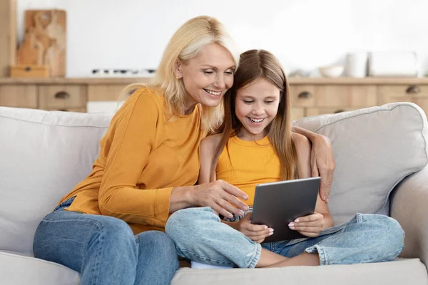 快乐美丽的老年妇女祖母和可爱的少女孙女一起坐在沙发上 在家里用数码平板电脑 看电影 网上购物 — 图库照片