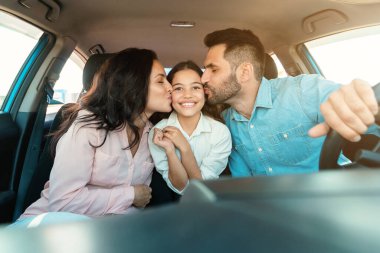 Aile gezisi. Mutlu ebeveynler birlikte araba sürerken kızlarını öperken anne, baba ve kız çocukları araçta vurulup arabayla seyahat etmekten zevk alıyorlar.