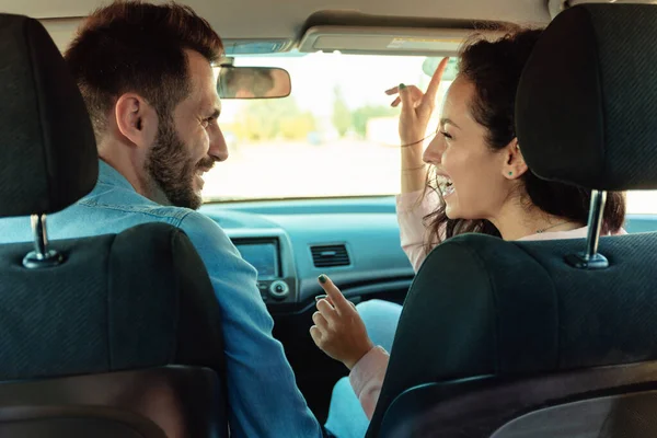 Happy couple sitting in car and singing, enjoying road together, rear view. Driver man and female passenger listening to favorite song in new automobile
