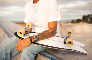 Kaykaycı adam antrenman için parkta oturuyor, patenini tutuyor, idman sonrası dinleniyor, yakın plan, kırpma...