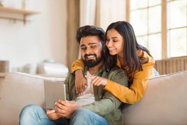 Boş zamanların teknolojisi. Hintli çift dijital tablet kullanıyor, arkadaşlarıyla görüntülü görüşme yapıyorlar, evdeki kanepede dinleniyorlar, boş yer var. Hindu erkek ve kadın modern aletlerle rahatlıyorlar.