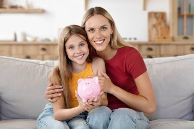 Finansal okuryazarlık. Anne, çocuk kızına para tasarrufu yapmayı öğretiyor. Ekonomi planı aile bütçesi ile kazanç sağlıyor. Dost canlısı anne ve çocuk evde pembe kumbara tutuyorlar.