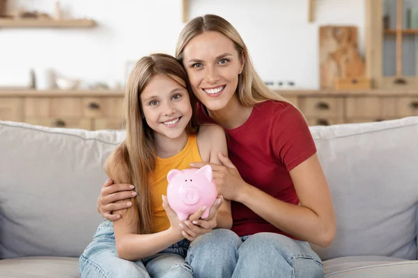 Financial literacy. Parent mother teach child teenager daughter girl to manage finances save money spend earnings with economy plan family budget. Friendly mom and kid holding pink piggybank at home