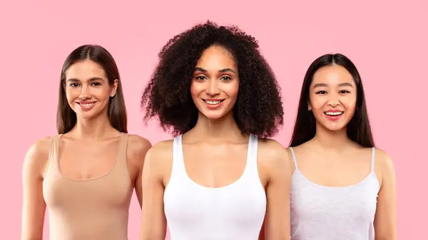 Diversity and natural beauty concept. Young multiracial ladies posing in casual and smiling at camera over pink background, studio shot, panorama