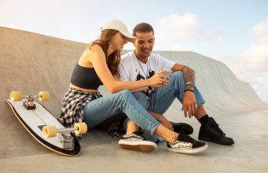 Avrupalı çift kaykay rampasında oturuyor, telefon kullanıyor, internette sörf yapıyor, özel ders ve boş alan arıyor. Mutlu patenciler cep telefonuyla dinleniyor.