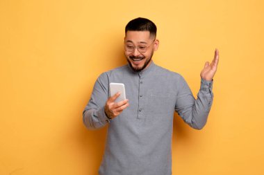 Harika bir uygulama. Harika Asyalı Genç Adam Heyecanlı Akıllı Telefon Ekranına Bakıyor, Mutlu Milenyum Adamı Çevrimiçi Kazanan ya da İyi Haberleri Kutluyor, Sarı Stüdyo Arkaplanının başında duruyor, Boşluğu Kopyala