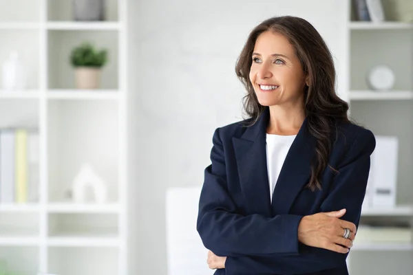 stock image Confident smiling beautiful brunette long-haired middle aged woman in forma outfit manager posing at white modern office, looking at copy space. Career, job opportunities in 50s concept