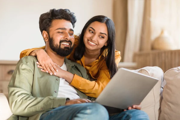一緒に家でラップトップを使用して幸せな若いインドのカップル ヒンドゥーの配偶者はリビングルームでコンピュータとソファーで休暇を過ごしながら オンラインで買い物をしたり 休暇を予約したり スペースをコピー — ストック写真