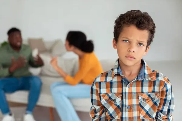 Family crisis. Unhappy little boy looking at camera while his angry parents fighting on the background at home, selective focus on depressed child feeling lonely during mom and dads divorce