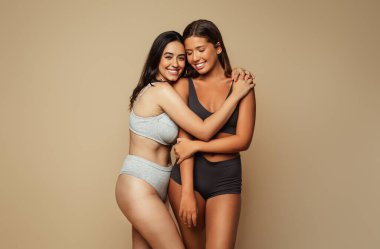 Neşeli bin yıllık Latince, iç çamaşırlı Arap kadınlar, bej arka planda, stüdyoda izole edilmiş. Kendini sevme motivasyonu, spa tedavisi ve zindelik, sağlık, cilt bakımı, doğal güzellik.