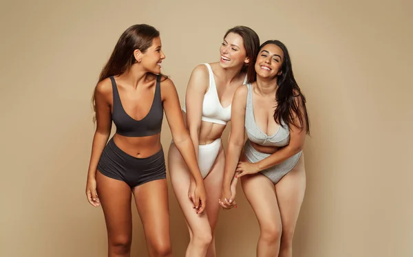 Group of laughing millennial different body and ethnicity women in underwear have fun, enjoy body care, isolated on beige background, studio. Motivation self love, wellness beauty and female power