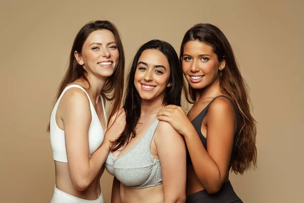 Cheerful pretty millennial diverse women in underwear enjoy beauty care, isolated on beige background, studio. Self love, body positive, wellness, healthy natural skin care, lifestyle